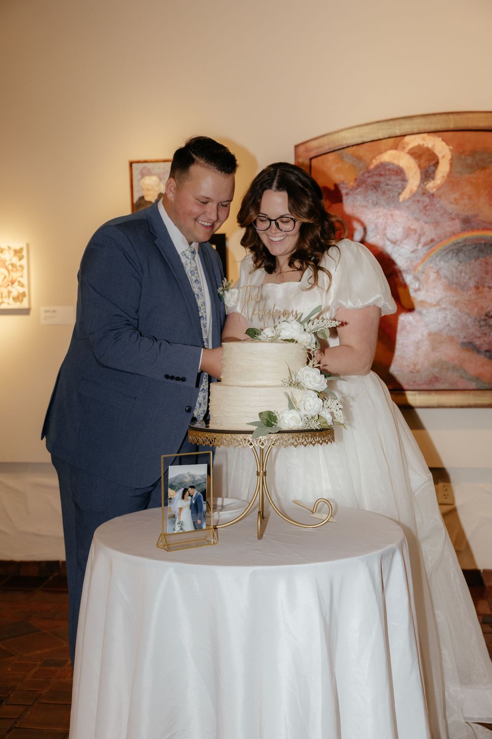 Bride and groom cutting their white two-tier wedding cake on a gold stand at their reception.
