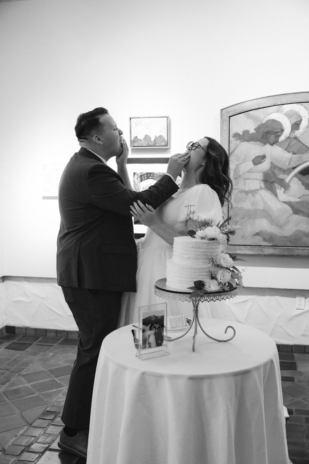 Black and white photo of bride and groom playfully feeding each other wedding cake at reception.