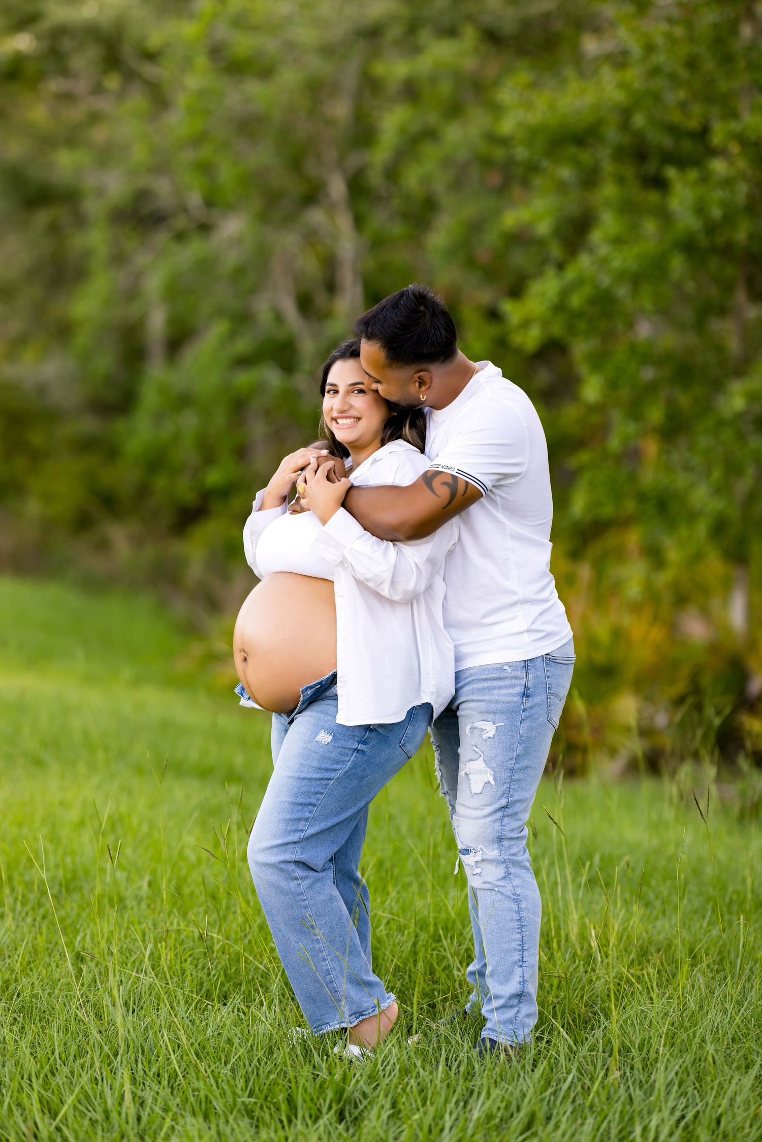 Couple embracing in outdoor setting with pregnant belly visible.