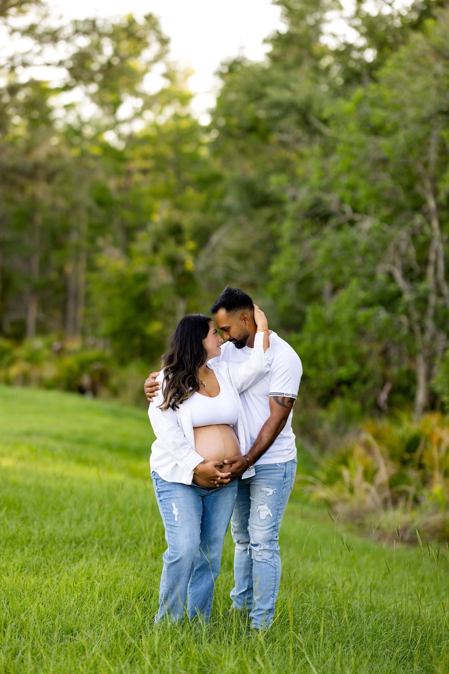 Couple embracing outdoors with pregnant belly between them.