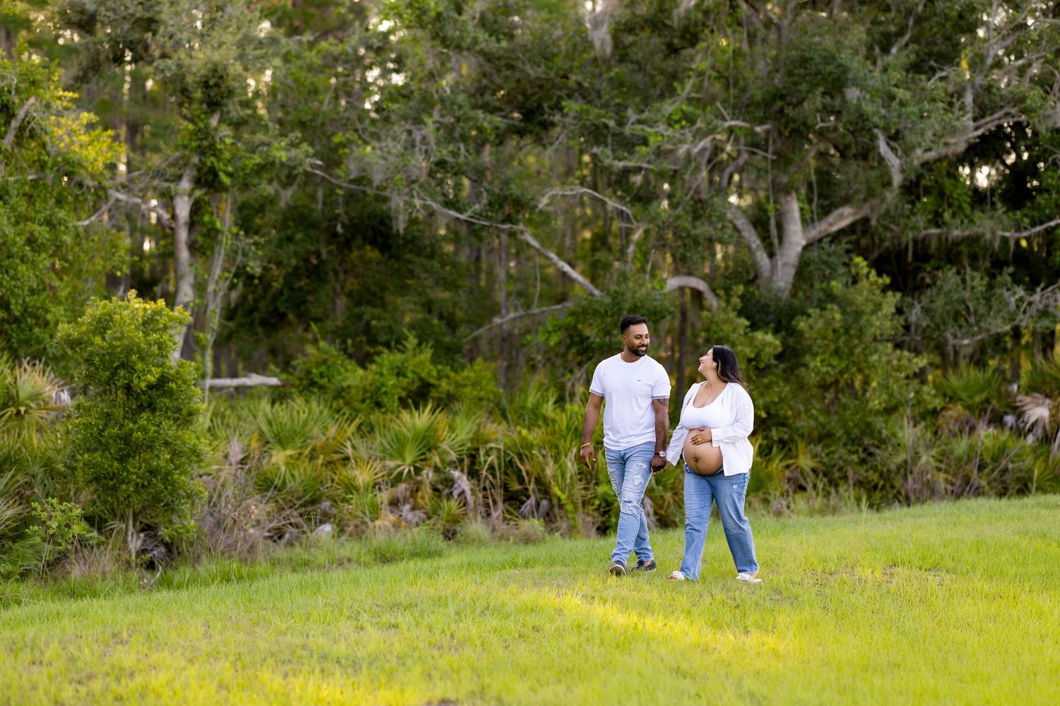 Couple walking together on grass with trees in background.