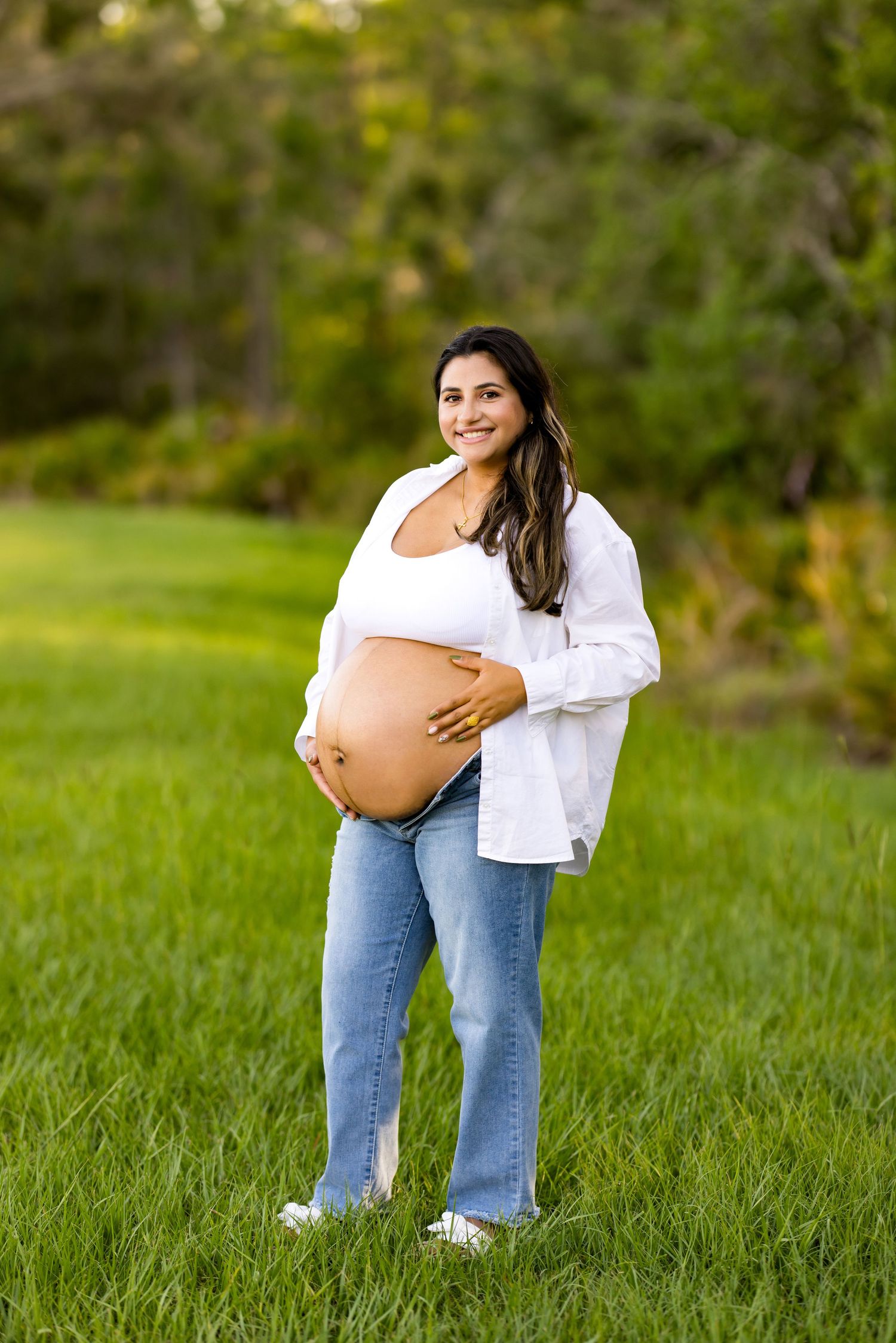 Pregnant woman in white shirt and jeans standing in grassy field.