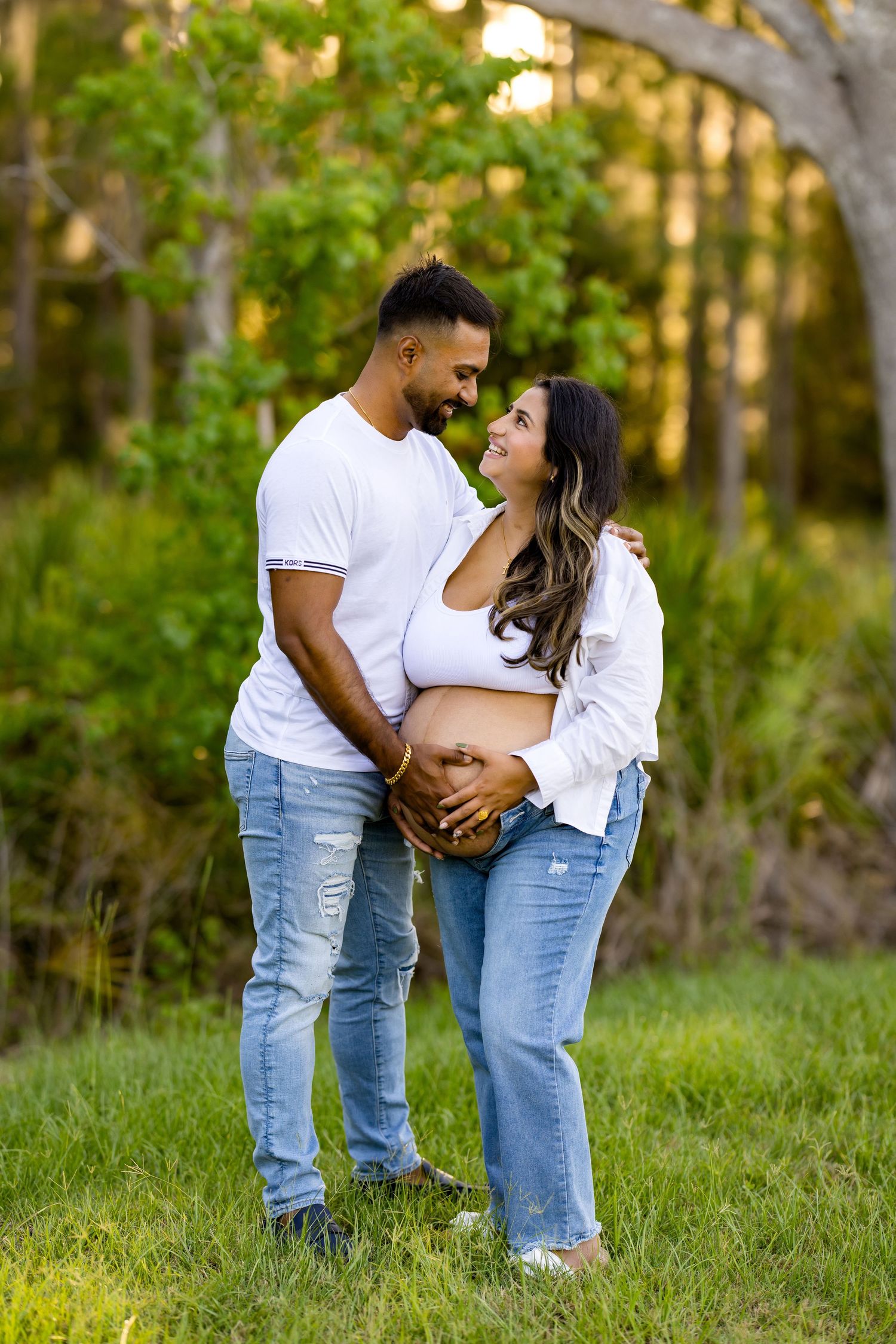 Couple in matching white shirts and jeans embrace lovingly in a sunlit outdoor garden setting.