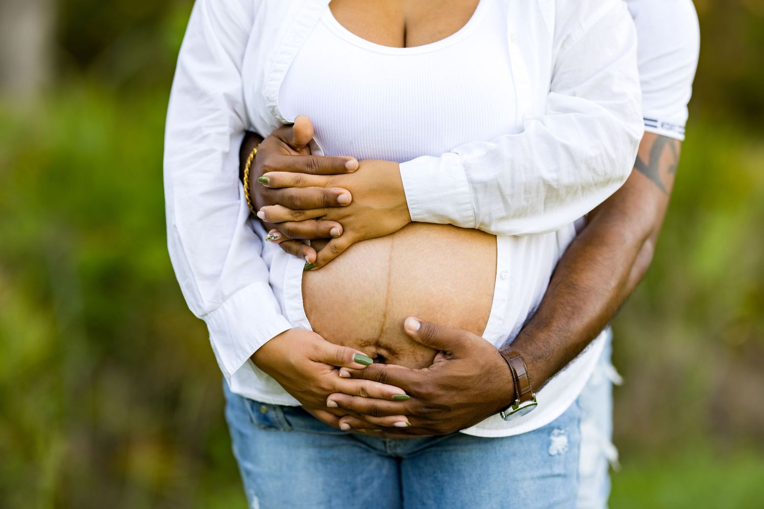 Tender outdoor maternity photo with couple in white shirts showing baby bump. DigitalMyst Photography