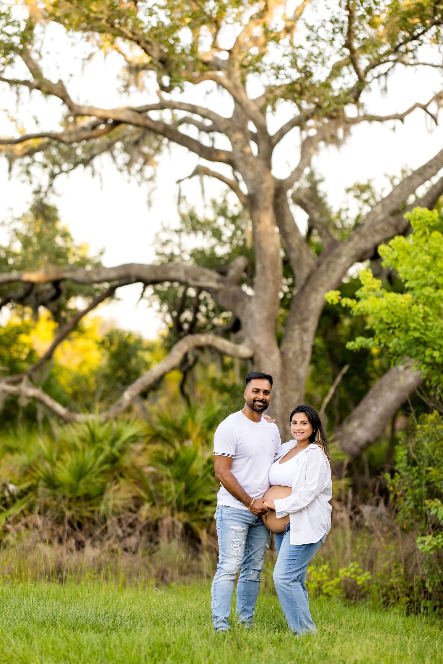 Couple shares intimate moment during outdoor pregnancy photoshoot among large oak trees. Photos by Tampa Photographer DigitalMyst Photograph
