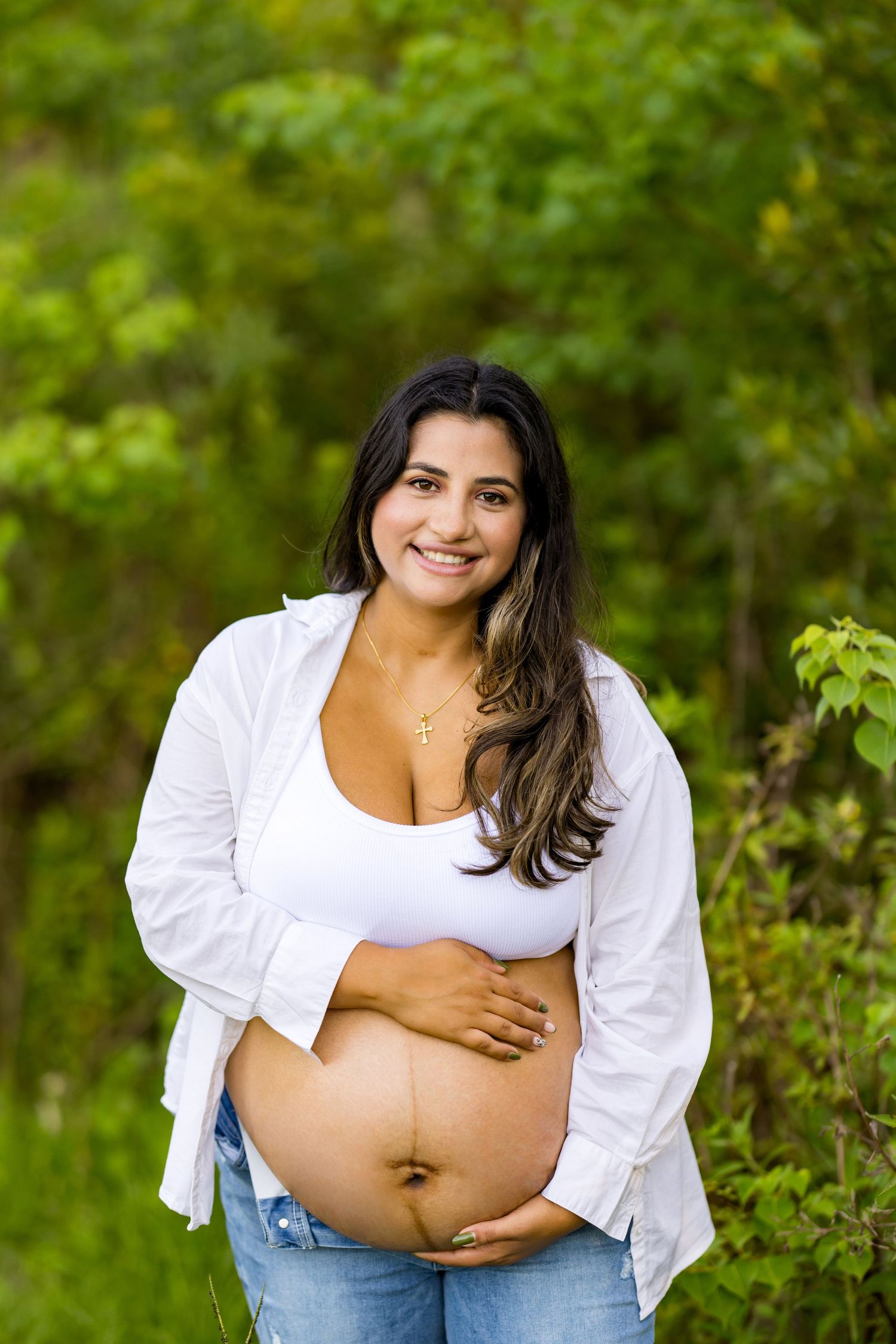Maternity photos showcasing baby bump in white shirt against green natural background.