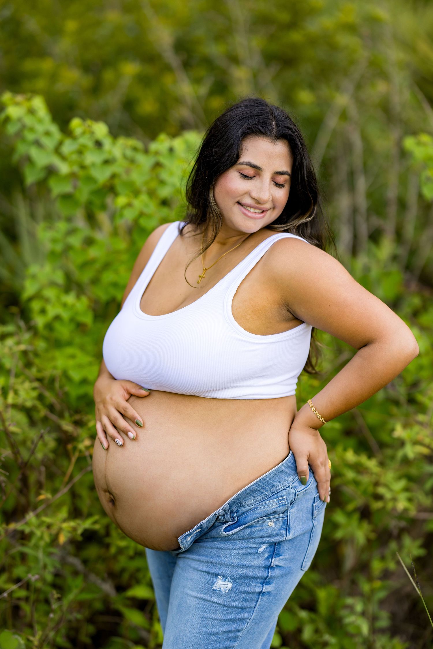 Solo maternity portraits showing baby bump against lush green outdoor backdrop.