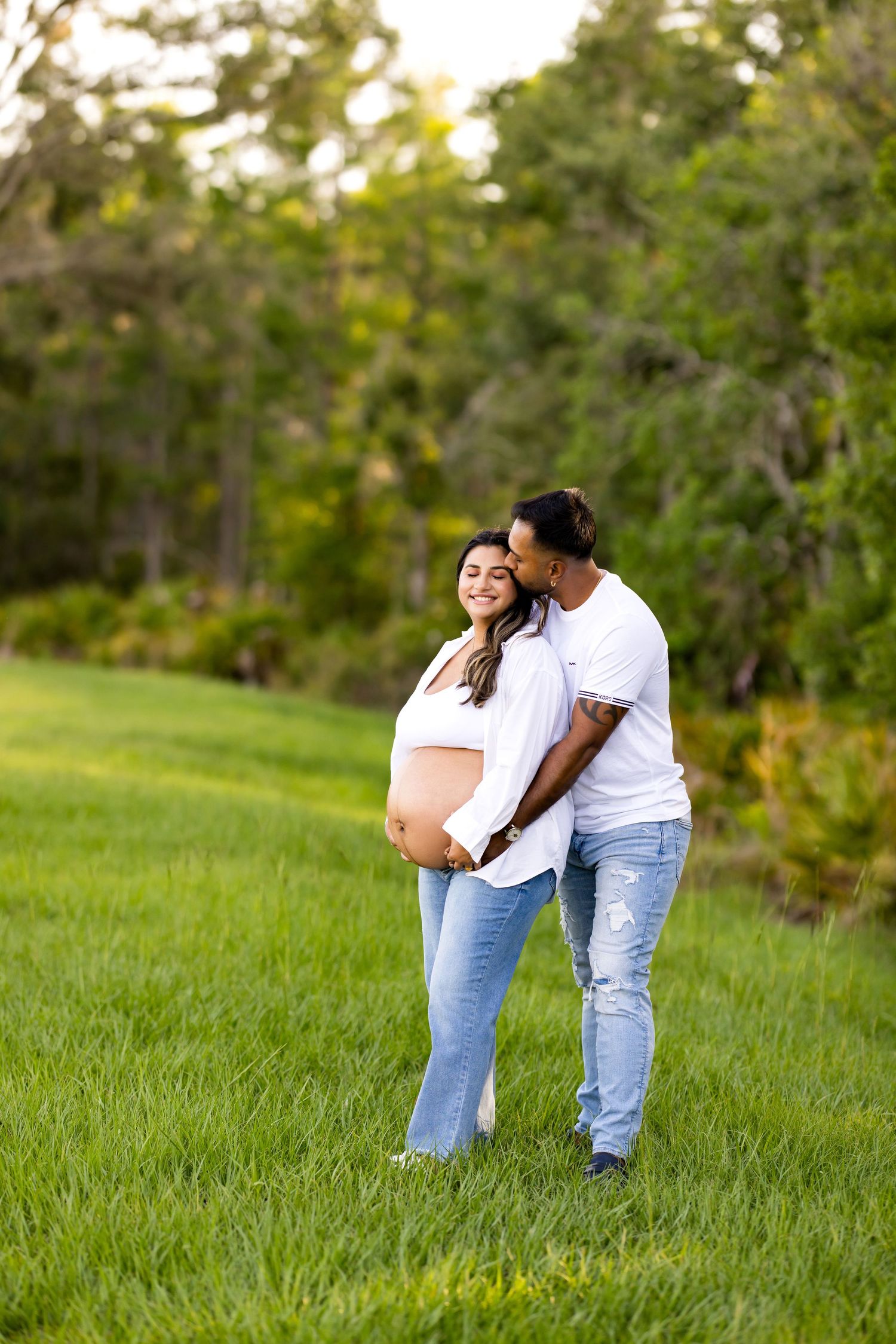 Couple embracing in a grassy field with trees in background.