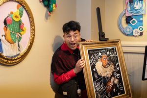 Person excitedly holding a framed artwork against a decorative wall with colorful art pieces in the background.
