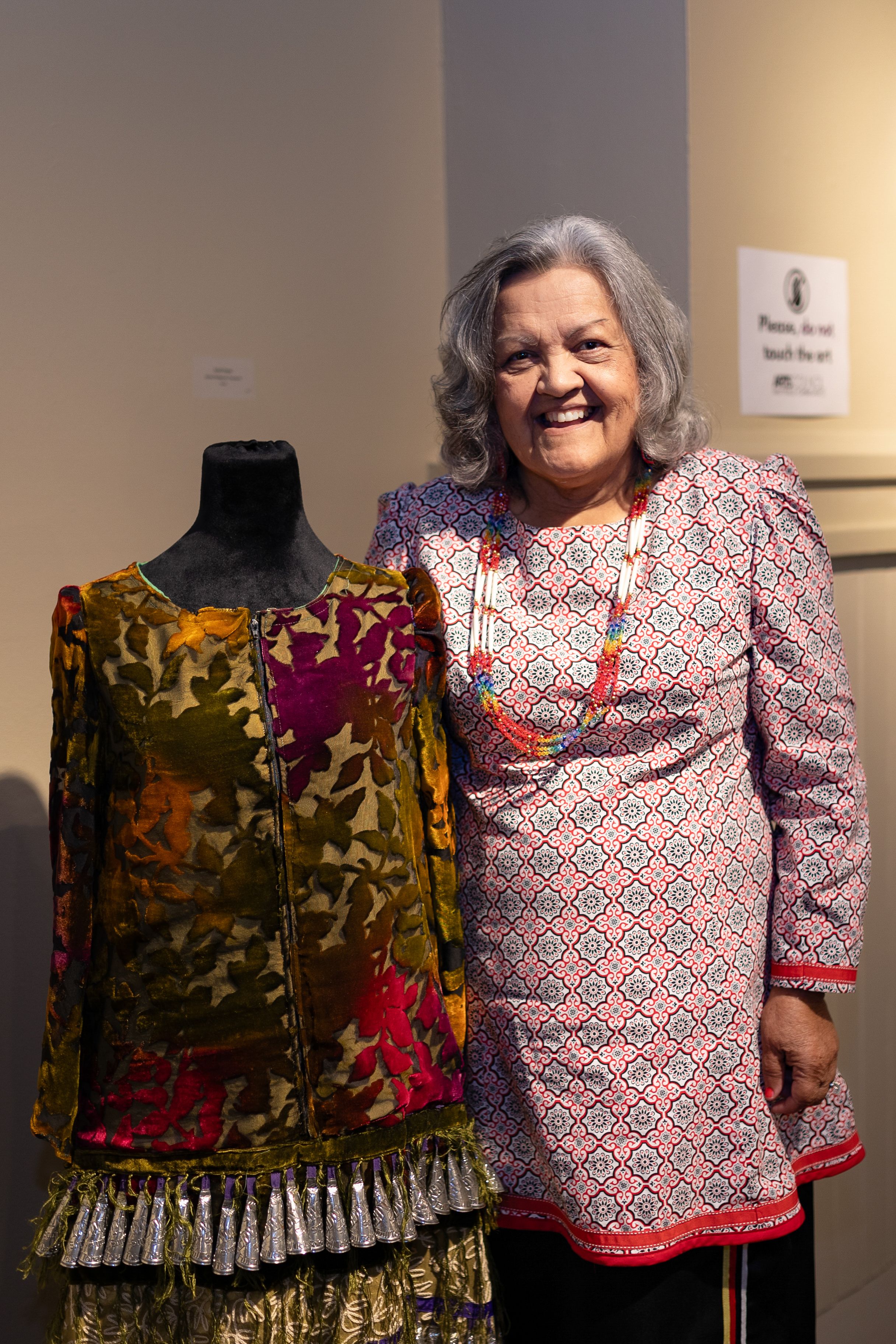 Traditional Native American dress displayed on mannequin next to creator in patterned dress.