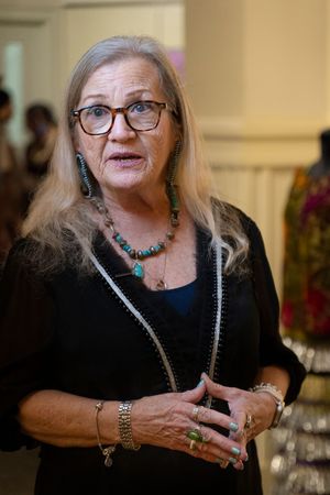 A person wearing glasses and turquoise jewelry stands in conversation while wearing a black outfit and silver necklaces.