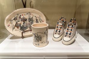 Elegant white porcelain dishes and cups with delicate Chinese-inspired landscape patterns displayed on museum shelves.