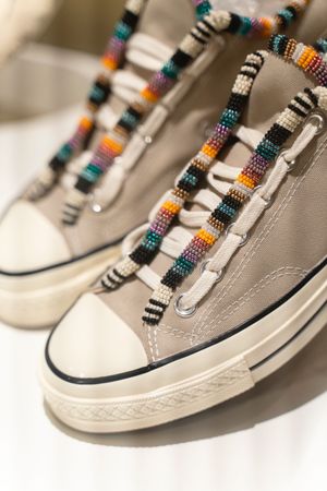 Close-up of casual sneakers with colorful striped laces featuring beaded embellishments.