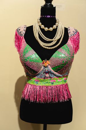 A colorful beaded and fringed costume top on a dress form with pearl necklaces.