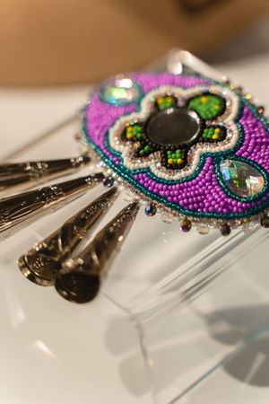 Detailed beaded barrette with purple and green floral design featuring crystals and metallic accents on a white surface.