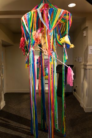A vibrant hanging art installation with multicolored ribbons and streamers cascading from the ceiling.