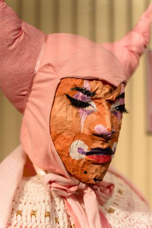 Theatrical mask with pink bonnet and dramatic makeup during performance or art exhibition.
