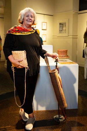 Person in black dress with colorful scarf displays traditional woven basket and rope at art exhibition.