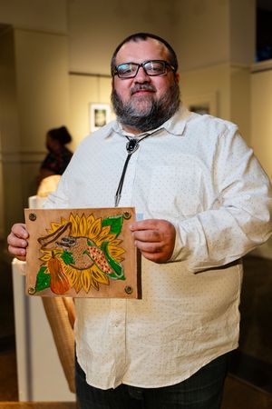 Person in white hoodie holding wooden art piece featuring colorful sunflower design.