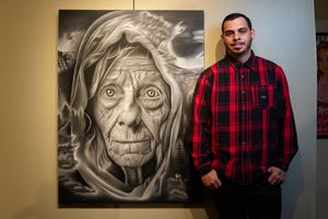 A person in a red plaid flannel shirt stands beside black and white wall art portraits in a gallery setting.