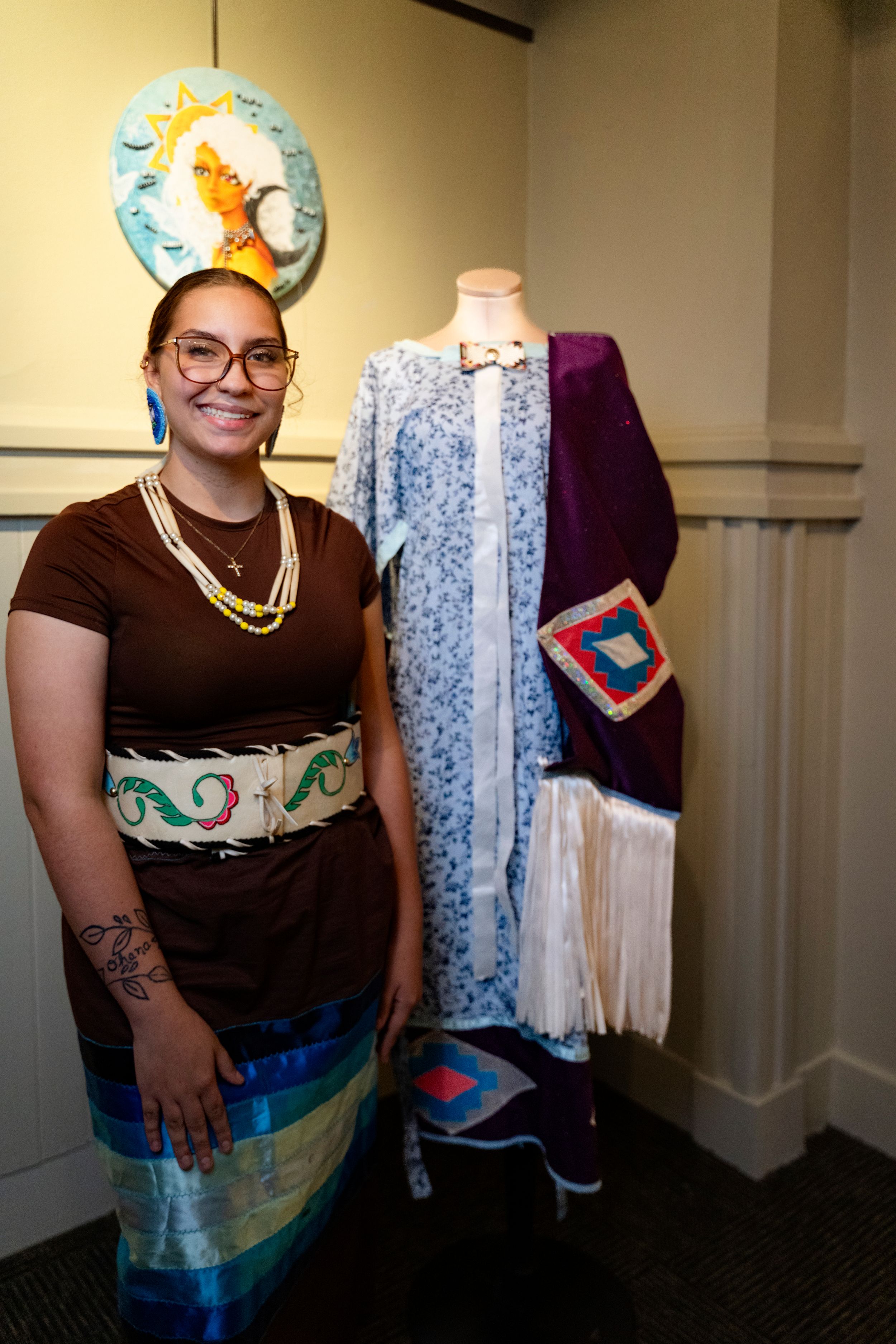 Person wearing brown dress with decorative belt stands next to mannequin displaying blue floral garment.
