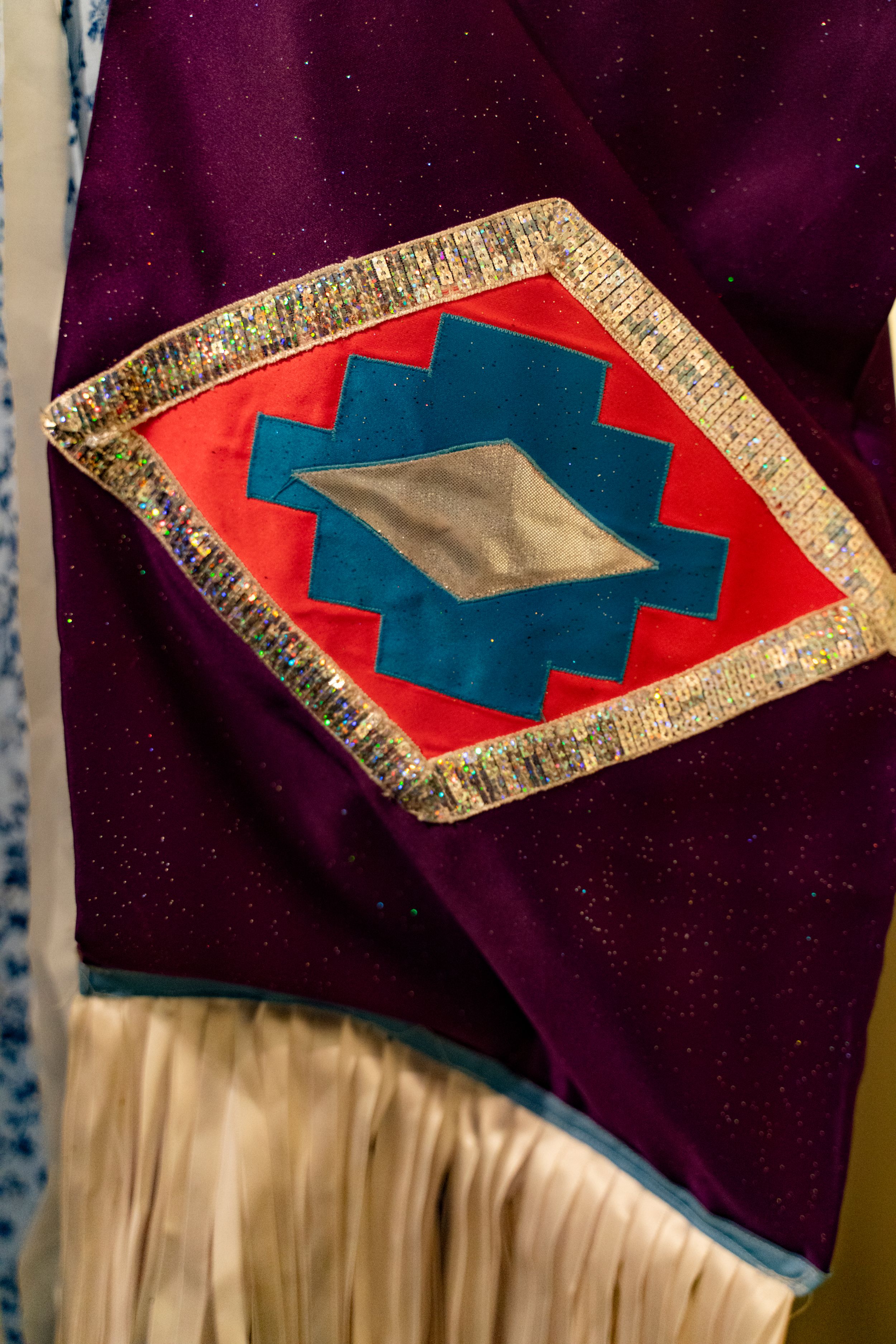 A decorative diamond-shaped Native American pattern in red, blue and gold on a purple fabric background.