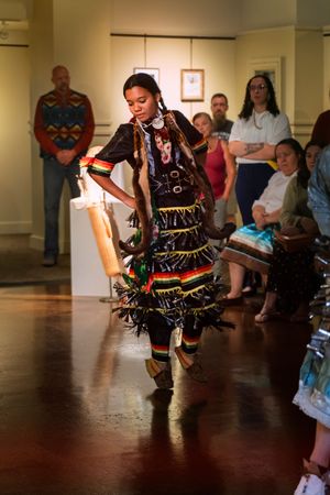 Traditional Native American dancer performs in colorful regalia during an indoor cultural event.