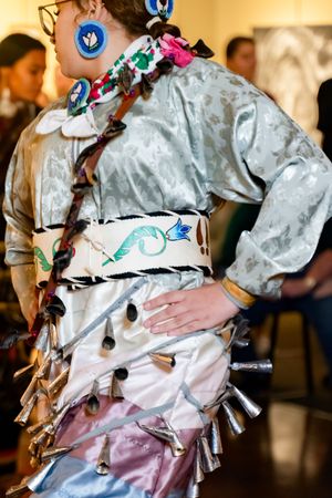 Close-up detail of a silver ceremonial costume featuring blue accents, fringe elements, and decorative embellishments.