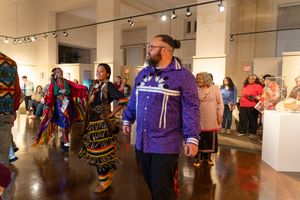 People in colorful traditional regalia gather for an art exhibition in a bright gallery space filled with displays.