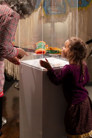 A child in a purple dress examines a colorful object displayed on a white pedestal in a museum setting.