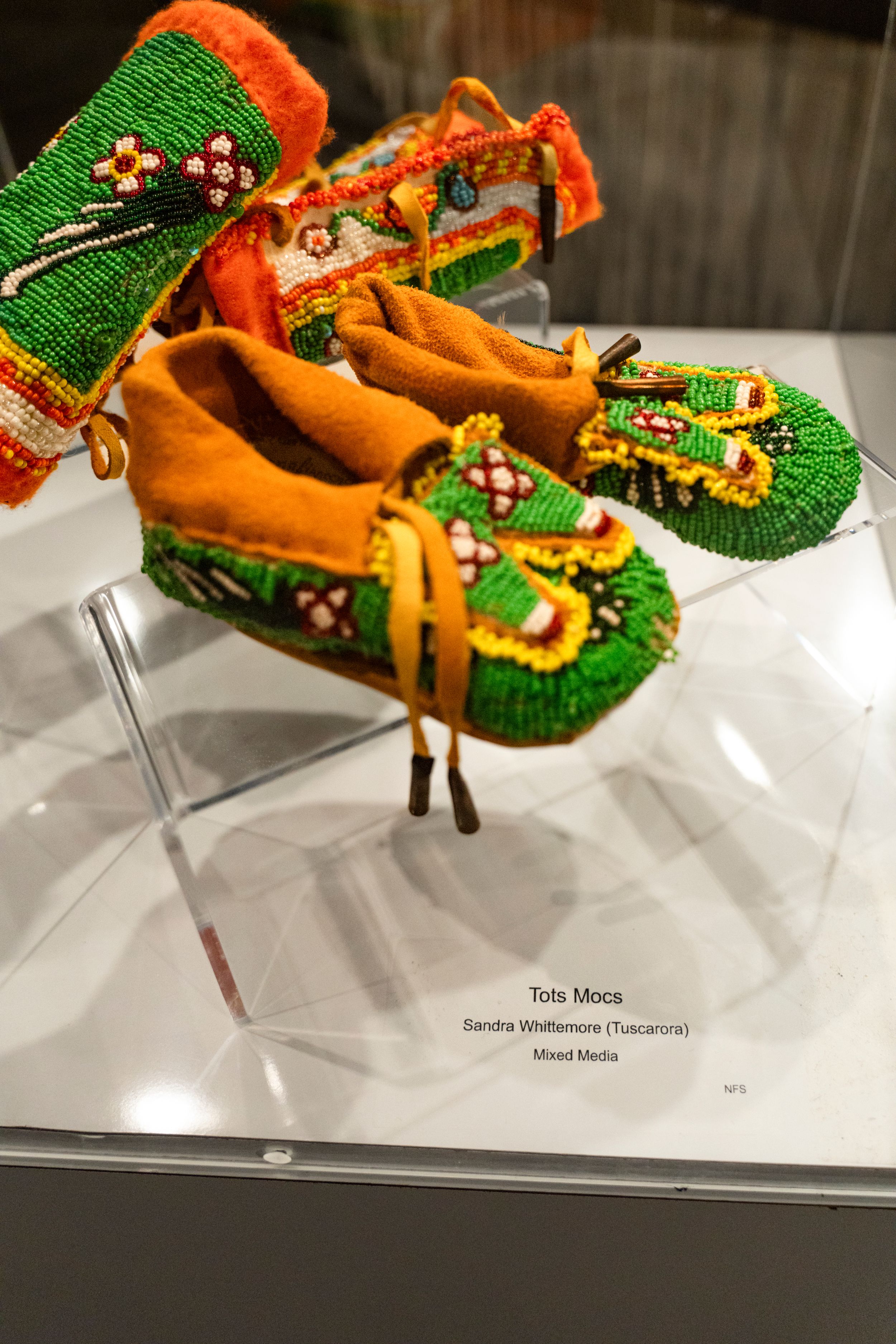 Traditional Native American moccasins with green and orange beadwork displayed in museum case.