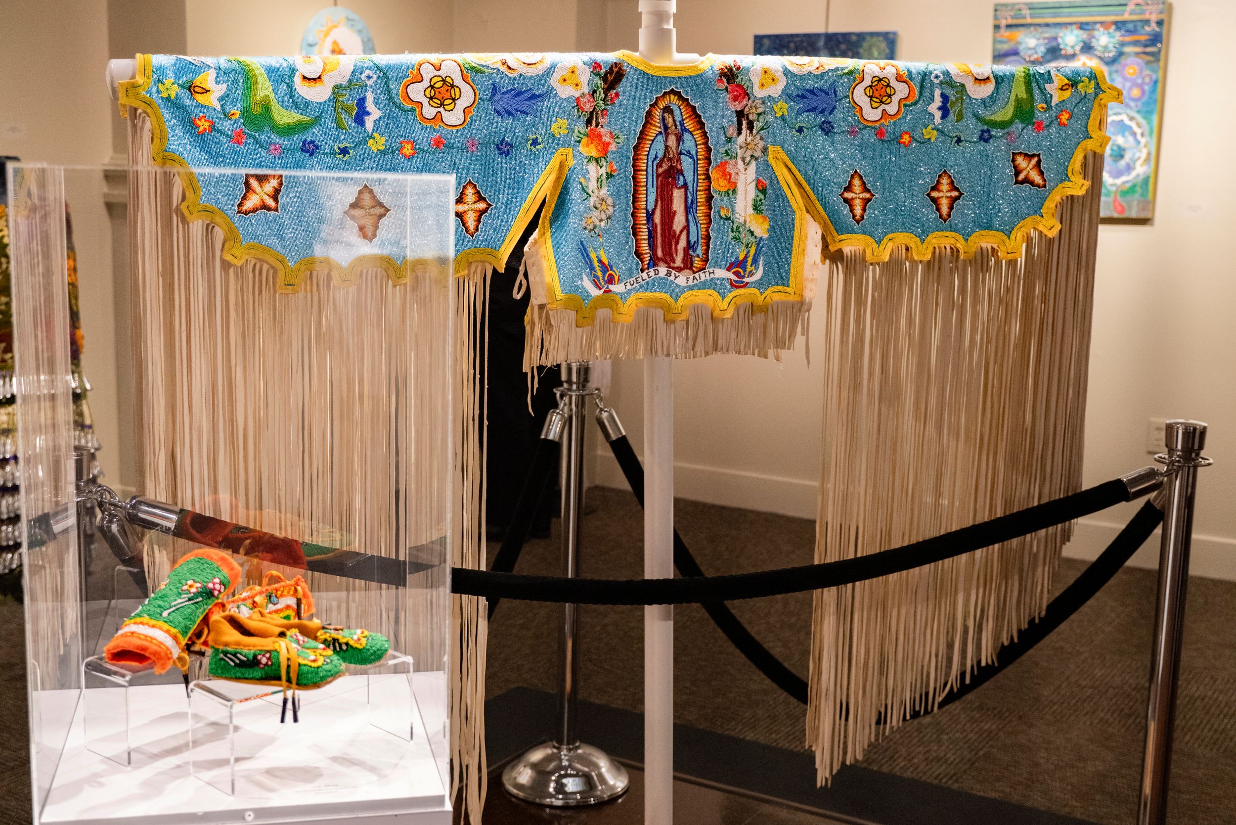 Colorful Dia de Los Muertos altar display with fringe decorations and floral banners against a light wall.