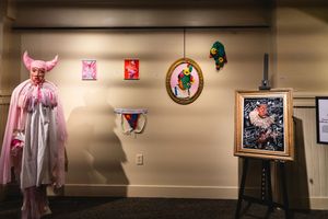 Art gallery wall displaying various framed pieces and a pink costume hanging against beige backdrop.