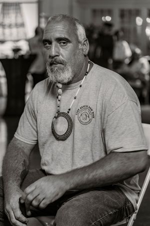 Portrait of person in gray shirt wearing circular medallion necklace in black and white.