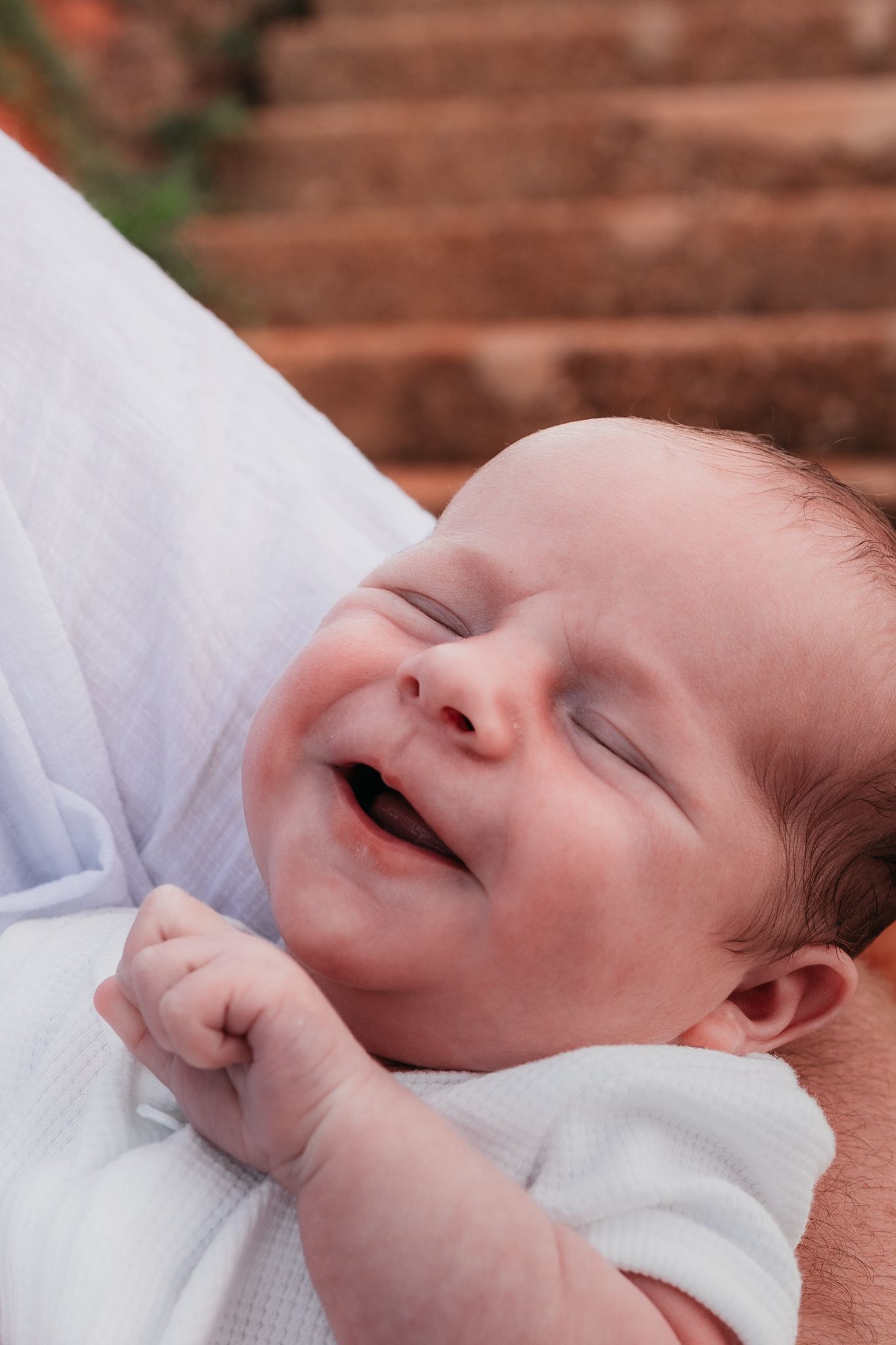 Beautiful newborn boy smiling in the arms of his father during family photoshoot