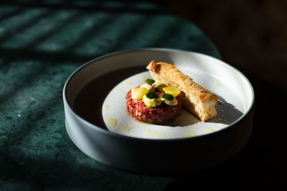 A gourmet open-faced burger with toppings served on a white ceramic plate against a dark green tablecloth.