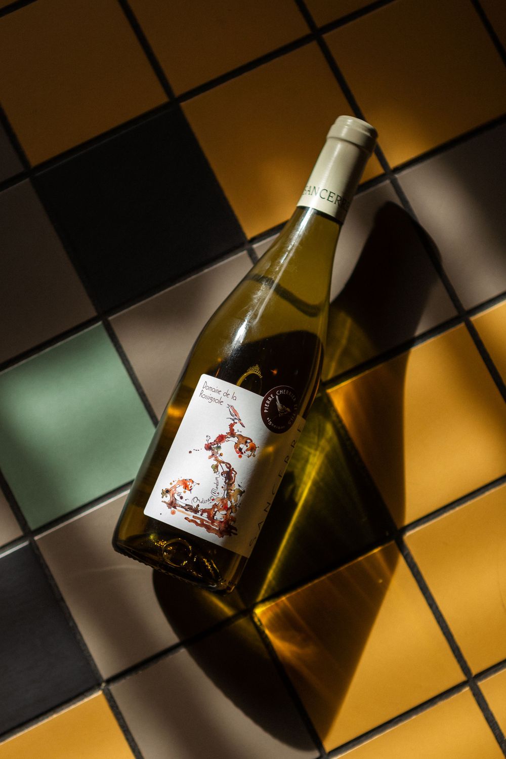 A white wine bottle lying on a colorful geometric tiled surface with dramatic lighting and shadows.