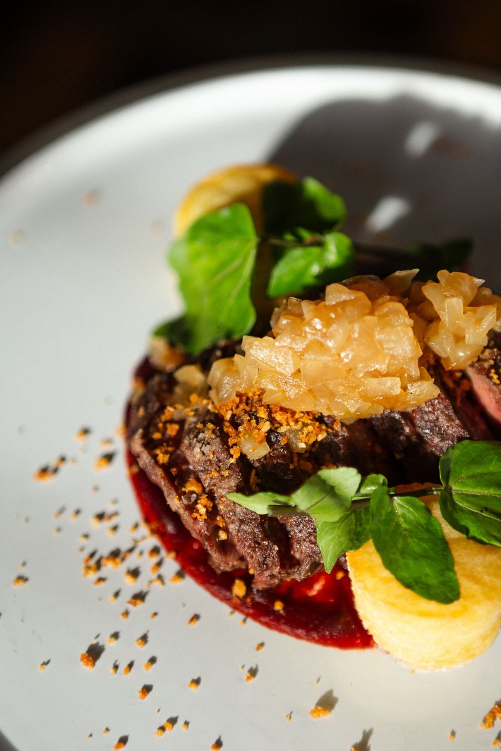 Gourmet beef dish plated with citrus segments, red sauce, fresh herbs and sprinkled garnish on white ceramic plate.