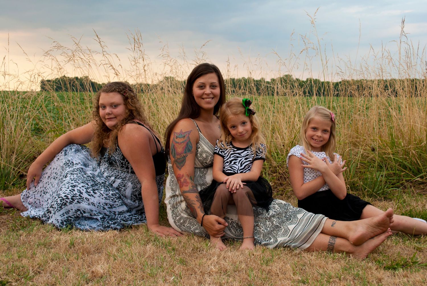 A group lounges together in a grassy meadow at sunset during a casual outdoor photo session.