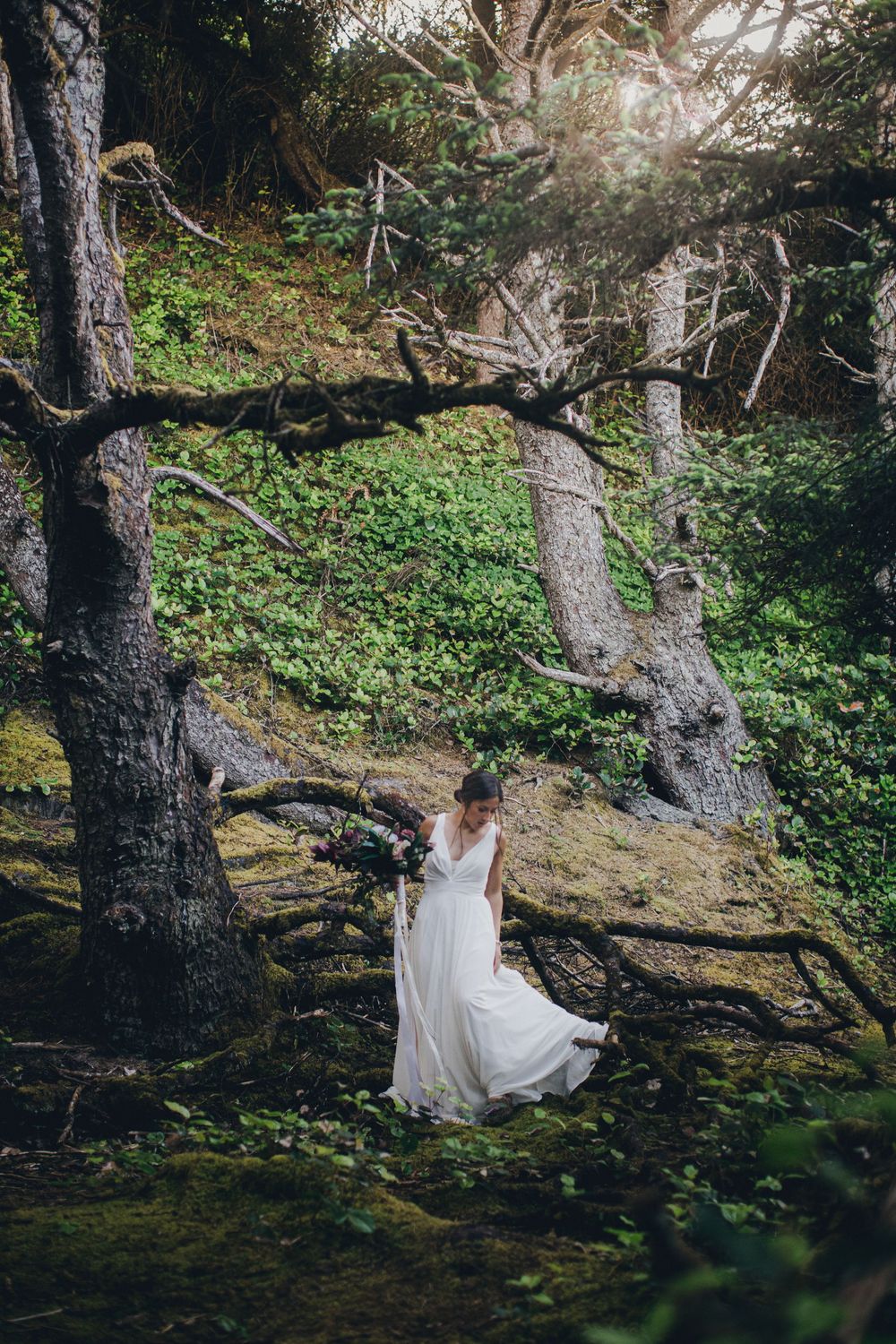 A flowing white dress catches sunlight beneath ancient gnarled trees in a mystical woodland setting.