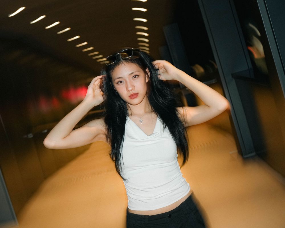 Person in white tank top and dark pants poses dynamically in tunnel-like space with dramatic lighting.
