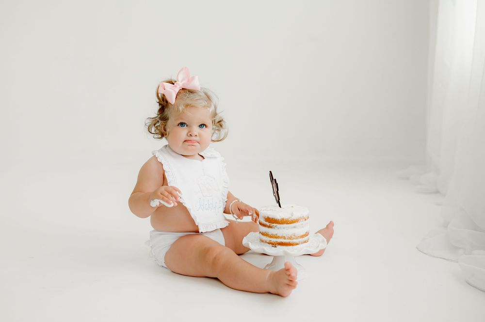 Four connected photos show a joyful smiling baby in a white bodysuit having a cake smash photo session.