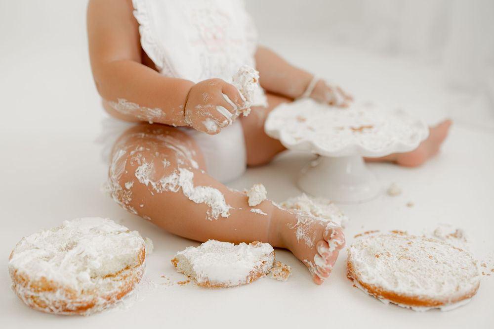 Small child's hands and feet playing with sprinkled powdered sugar and donuts on a white surface.