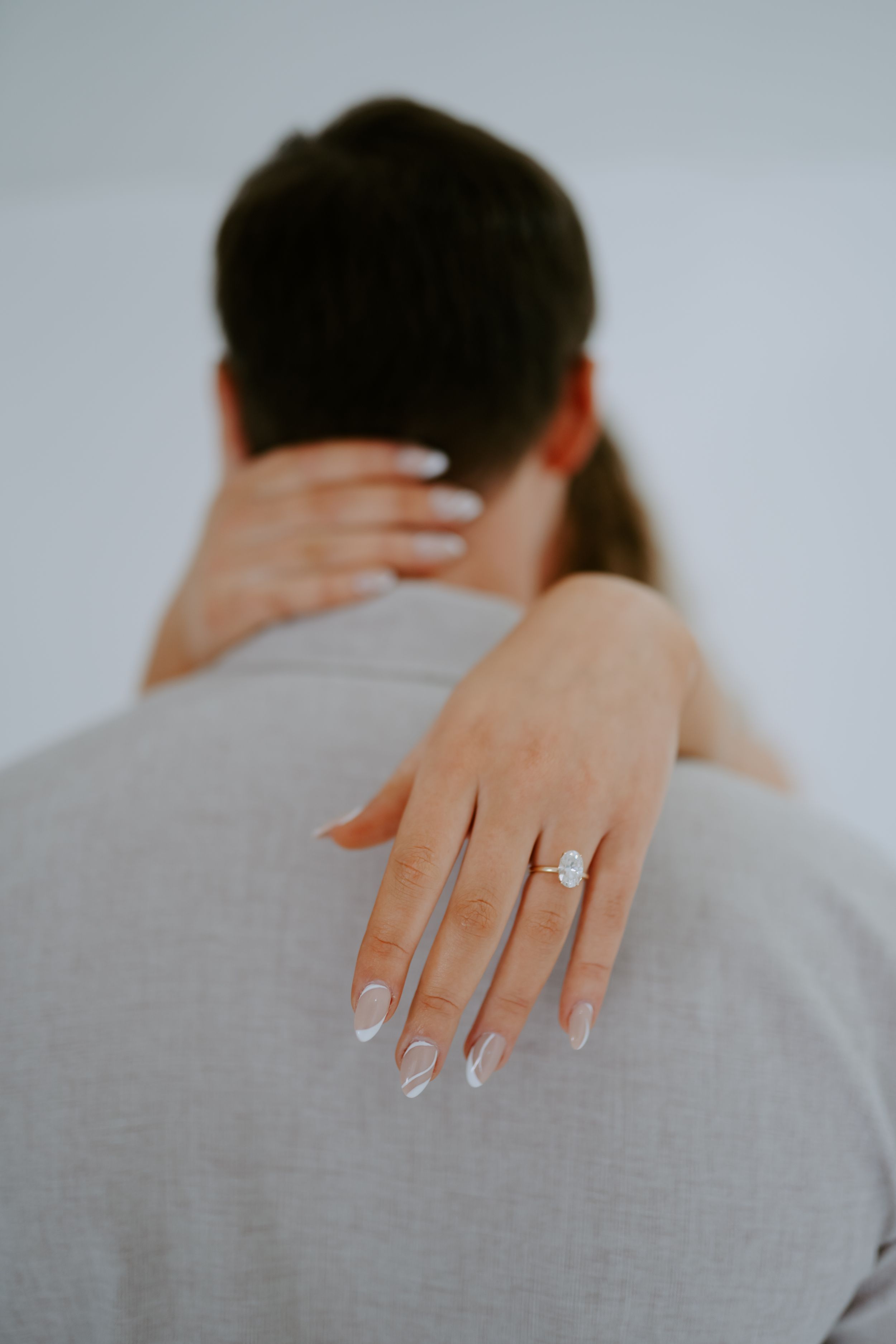 Detail shots focusing on hands with engagement ring and gentle touches against grey clothing.