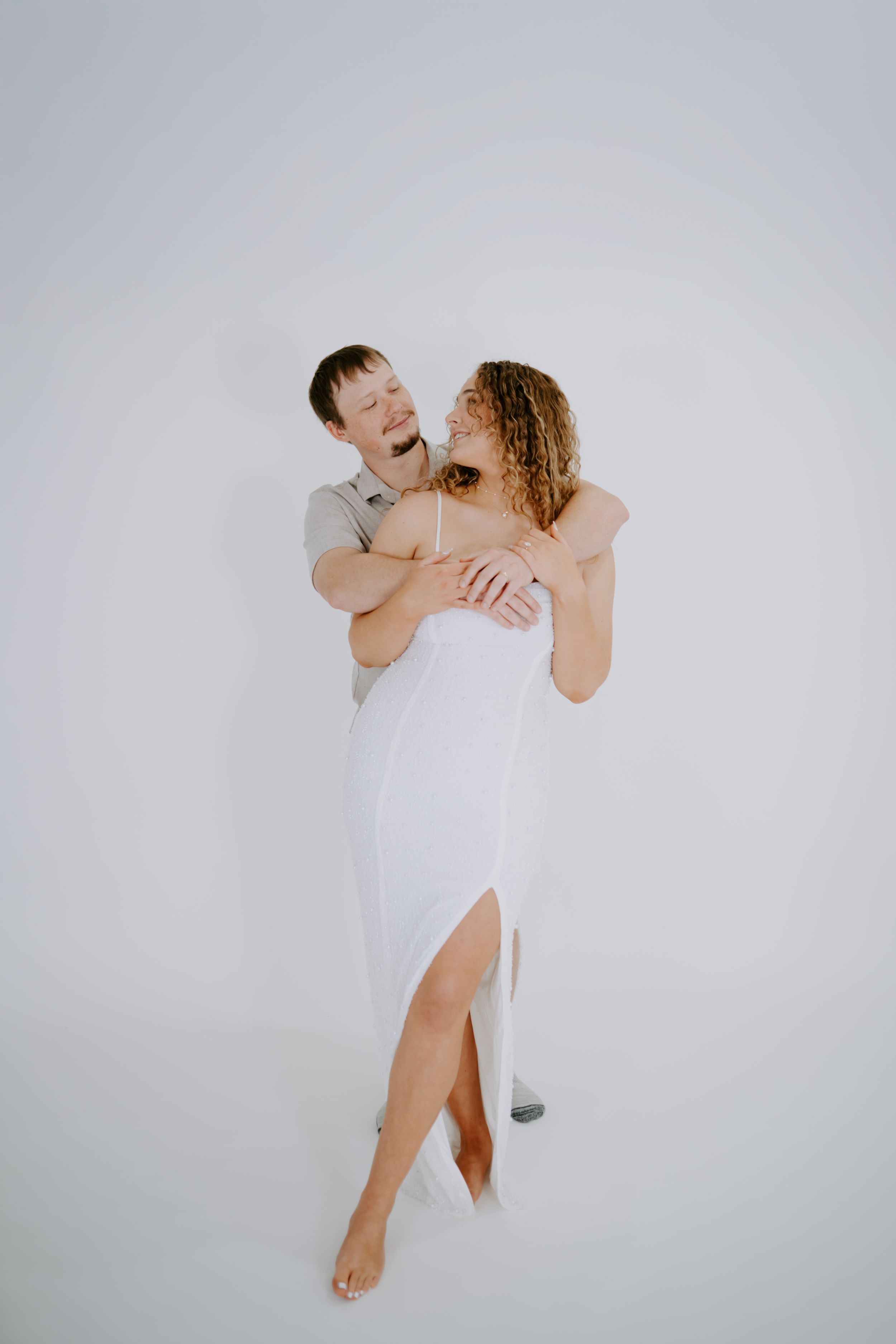 Minimalist studio portraits showing playful lifts and embraces in white attire.