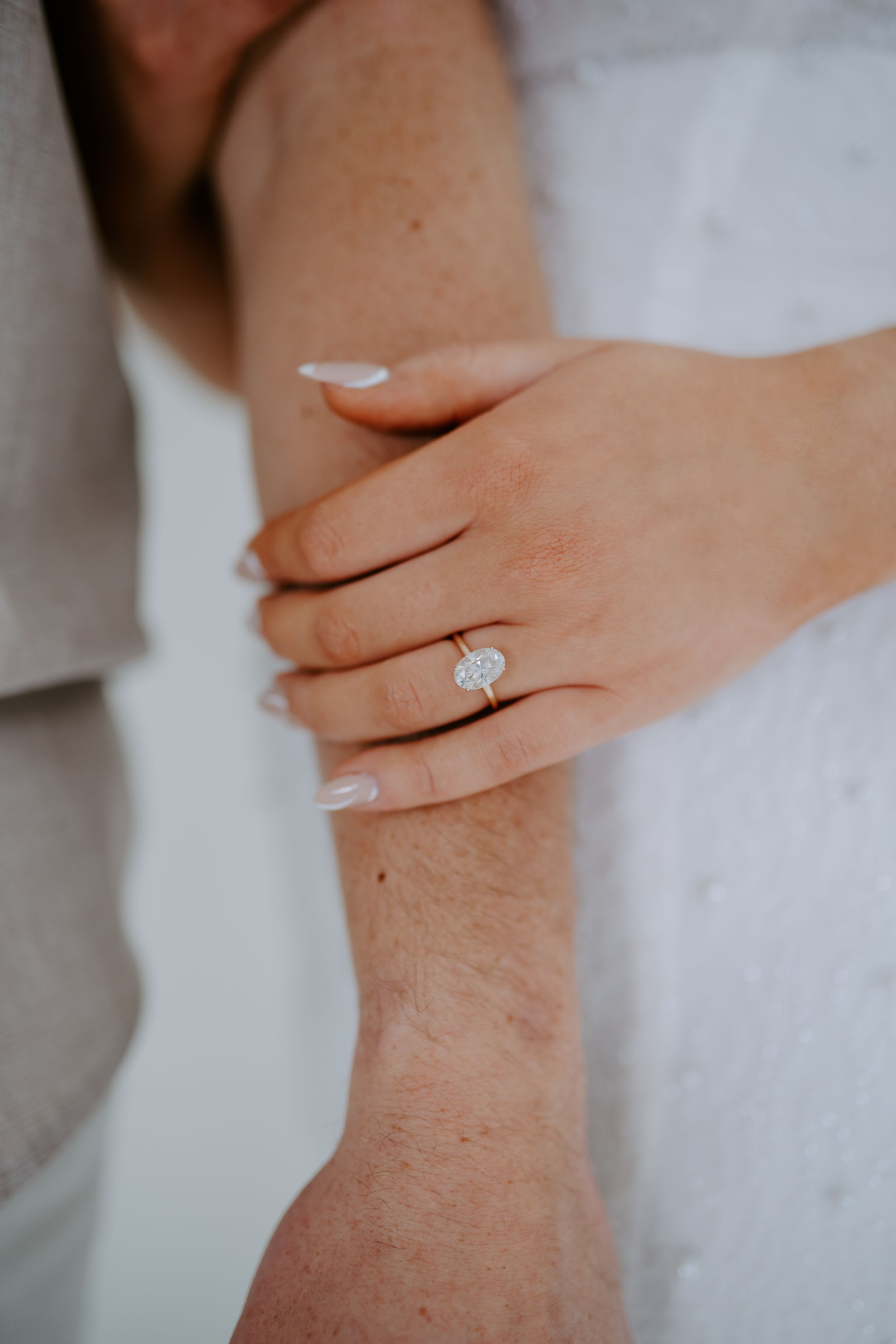 Detail shots of hands with engagement ring against white fabric texture.