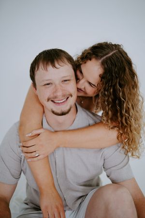 Candid couple portrait showing joyful laughter and embrace against white backdrop.