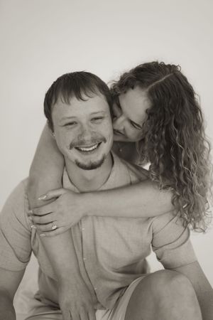 Black and white portrait of couple sharing intimate embrace against neutral background.