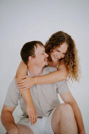 Intimate couple portrait showing playful piggyback moment against white background.