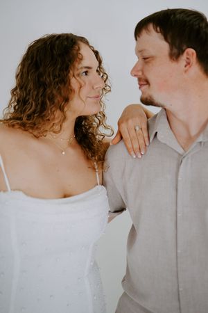 Romantic couple portrait with woman in white dress and man in grey shirt against light background.